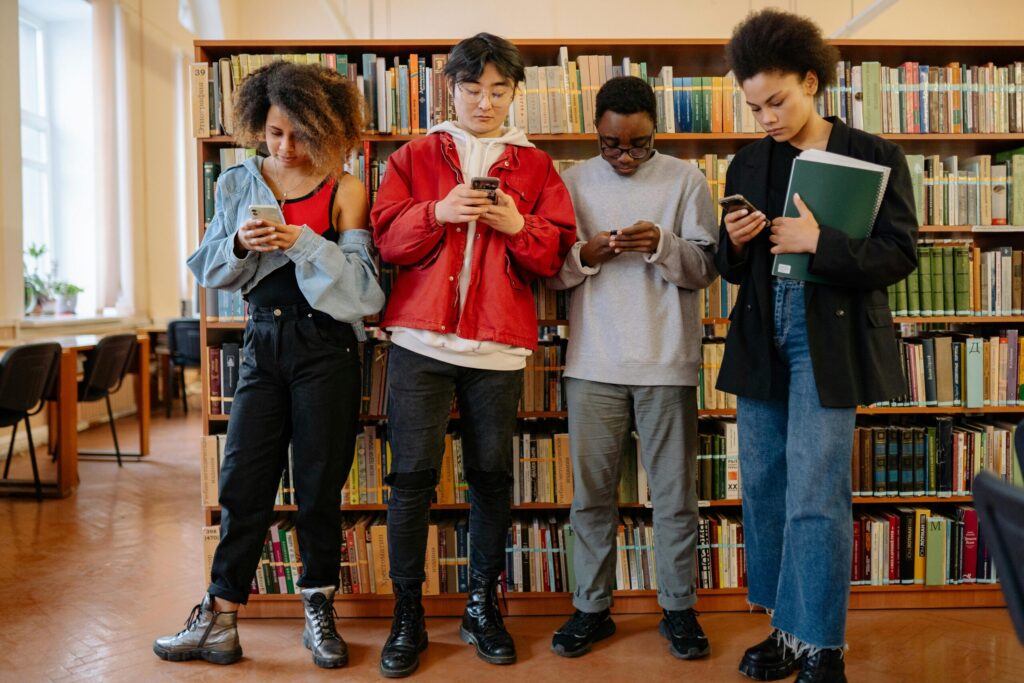 A group of university students using smartphones while standing in a library.